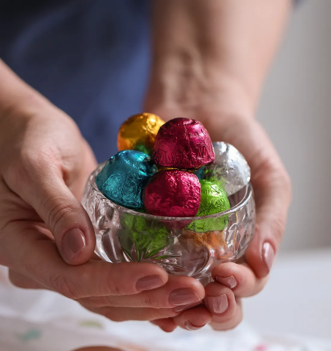 Mãos oferecendo uma taça de cristal com bombons embalados em papéis metalizados coloridos