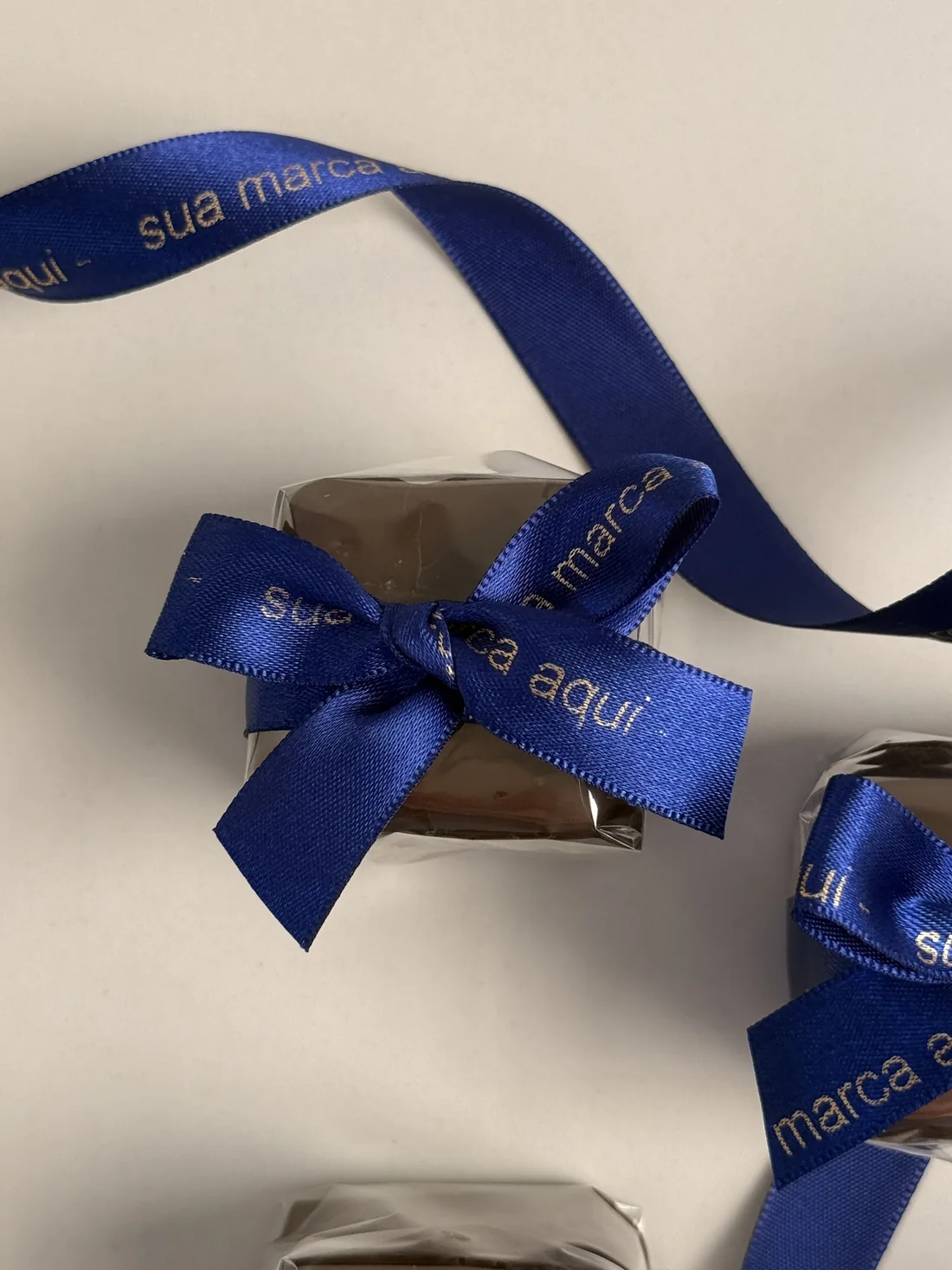 Pães de mel embalados e fechados com fita de cetim azul personalizada, onde se lê “sua marca aqui” em dourado